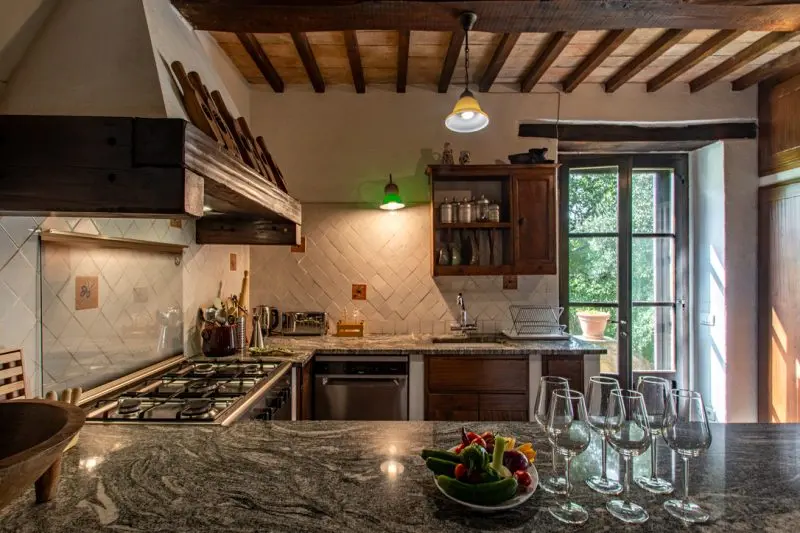 Rustic kitchen with exposed wooden beams, granite island, gas cooktop, and a glass door to the outdoors.